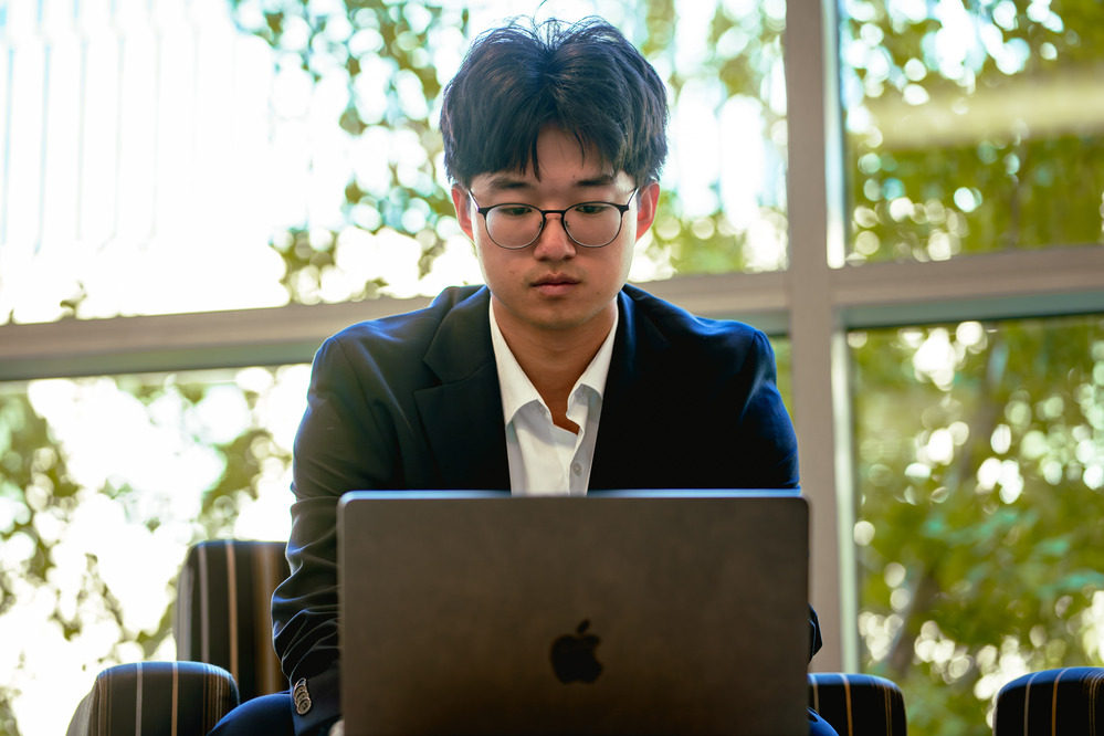 student sitting behind their laptop while in front of a window